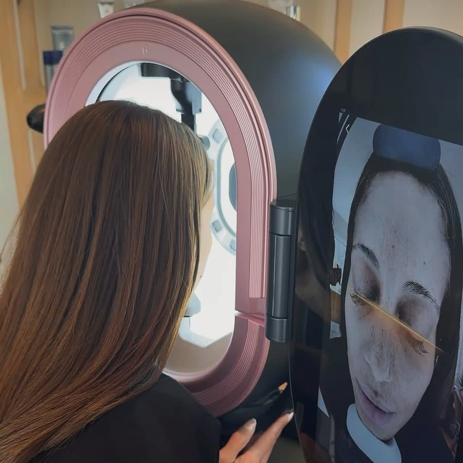A client at the skin analysis scanner, her scan on the screen beside her